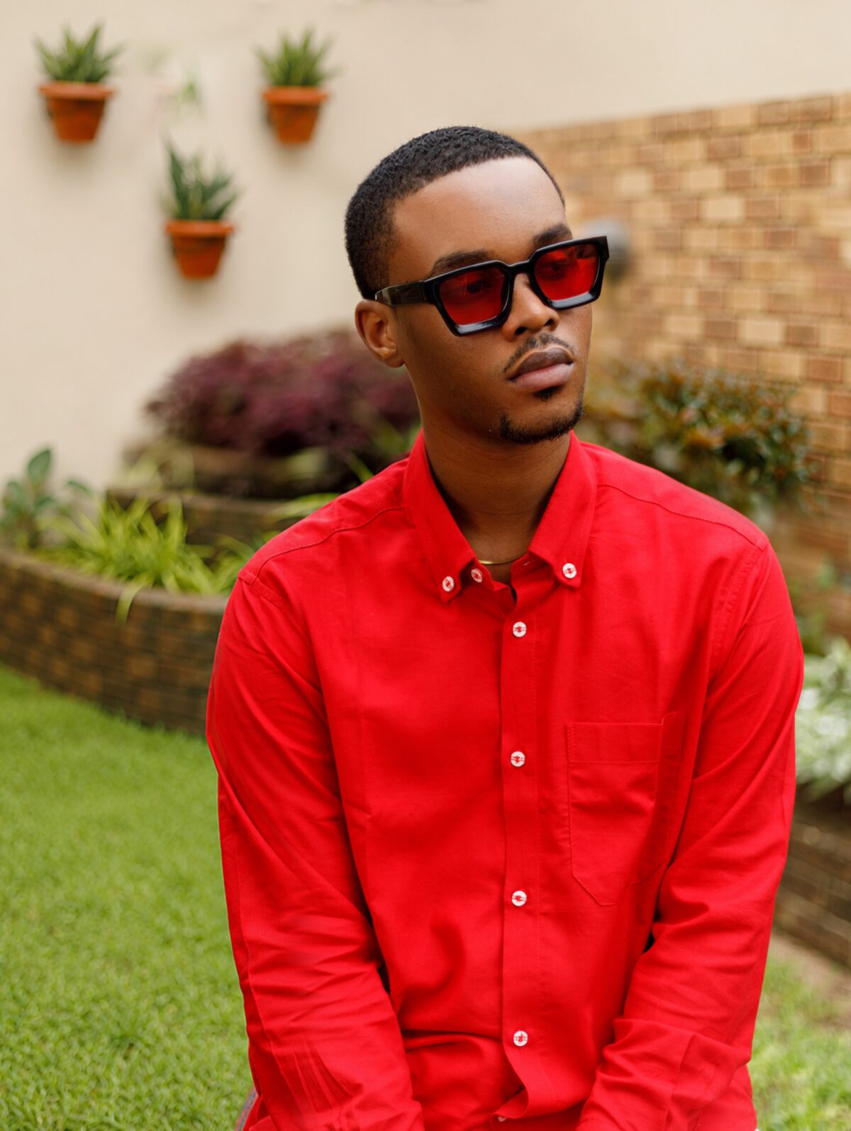 Mayowa Mula wearing a red shirt and red-tinted sunglasses in a garden.