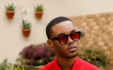 Mayowa Mula wearing a red shirt and red-tinted sunglasses in a garden.