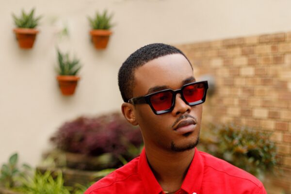 Mayowa Mula wearing a red shirt and red-tinted sunglasses in a garden.